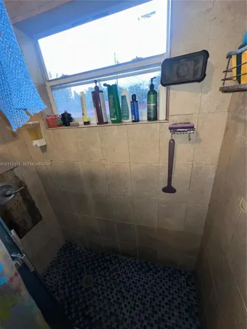Shower enclosure featuring large-format neutral-toned wall tiles, dark mosaic floor tiling, and an integrated horizontal tile shelf