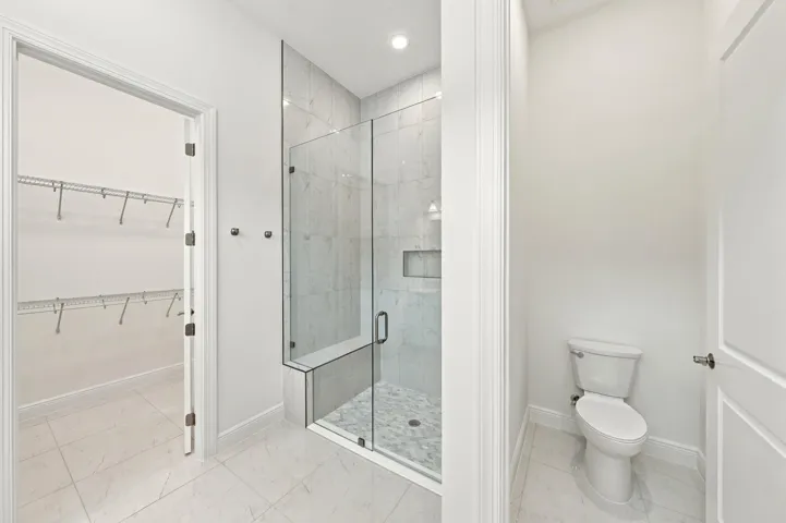 Primary bathroom frameless 96 inch glass shower with bench and upgraded tile to the ceiling with soft pebble shower floor, walk-in closet