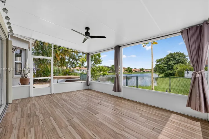 Screened-in lanai featuring wood-finish flooring, a ceiling fan, and large window panels overlooking the​​‌​​​​‌​​‌‌​‌‌​​​‌‌​‌​‌​‌​​​‌​​ water