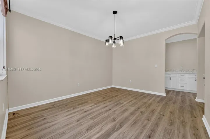 Interior space featuring wood-finish flooring, crown molding, a multi-light pendant fixture, and a built-in cabinetry unit with a countertop