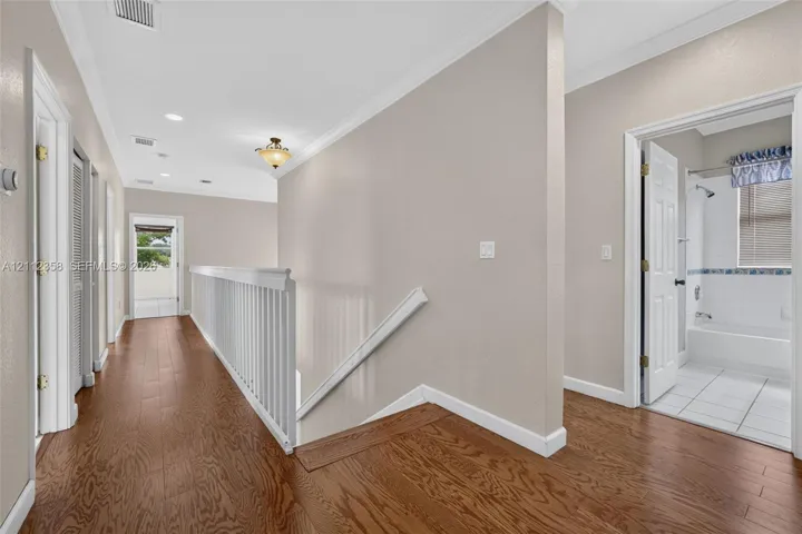 Hallway featuring wood-finish flooring, white crown molding, a decorative ceiling-mounted light fixture, and a white balustrade
