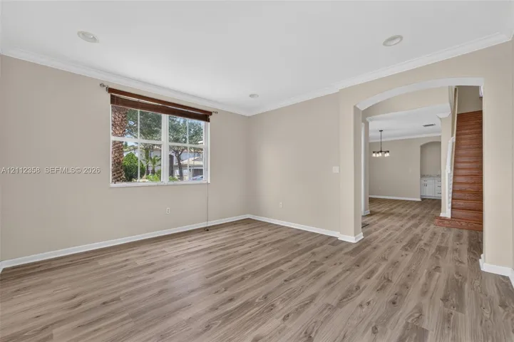 Open-concept space featuring wood-finish flooring, crown molding, recessed lighting, and a prominent arched entryway with wood-finish staircase