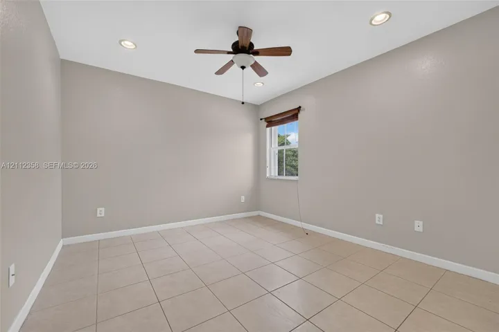 Neutral-toned room featuring large-format tile flooring, recessed lighting, a ceiling fan, and a single window with a wooden valance