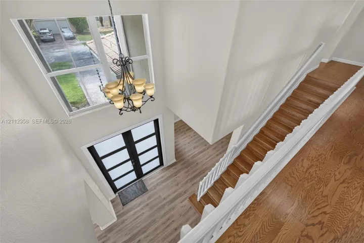 Double-height entryway featuring wood-finish flooring, a multi-pane glass door, a metal chandelier, and a staircase with white balusters