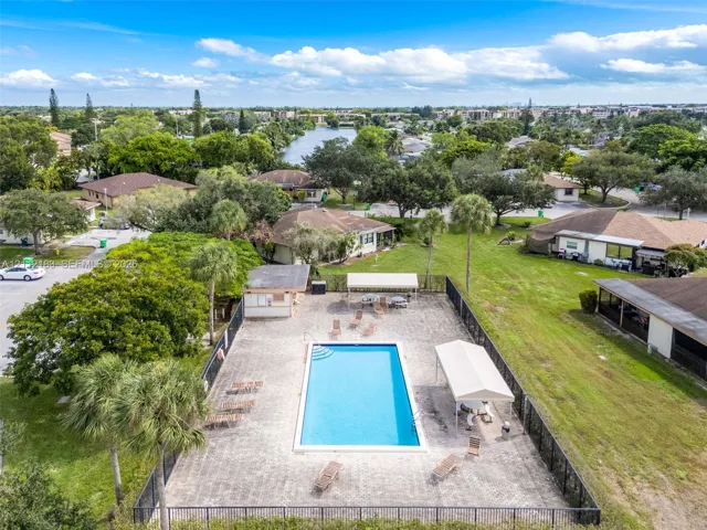 Fenced swimming pool with a paved deck, permanent poolside cabana, and mature perimeter landscaping