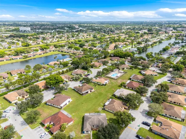 Aerial perspective featuring multi-unit residential structures, mature canopy trees, manicured lawns, and integrated water features