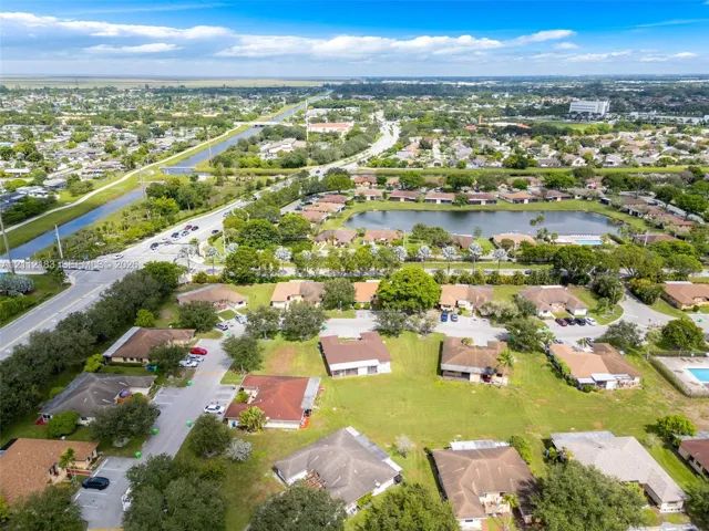Aerial perspective featuring established residential density, mature canopy trees, winding waterways, and prominent community pond
