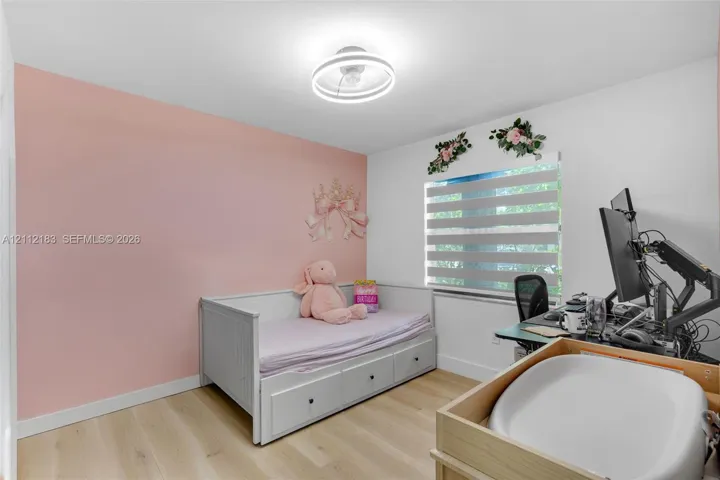 Bedroom featuring wood-finish flooring, a contemporary circular LED flush-mount light fixture, and horizontal zebra-style blinds