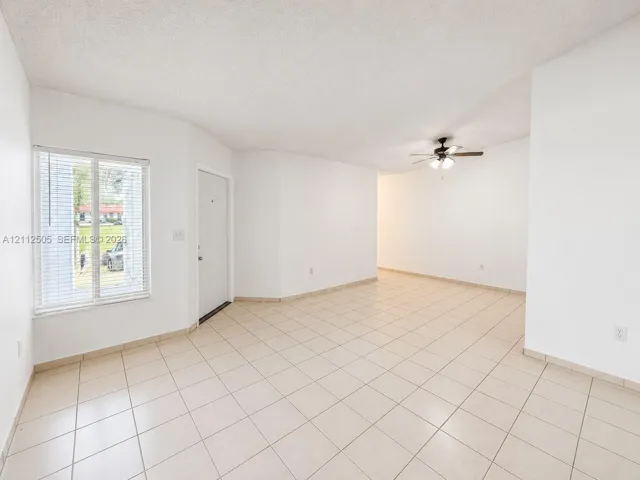 Neutral-toned tile flooring, single-pane window with horizontal blinds, and a ceiling-mounted light fixture with a fan