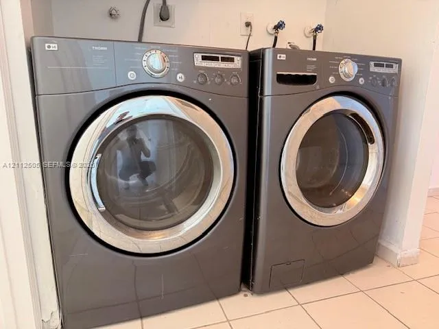 Front-loading, graphite-finish laundry appliances with metallic-rimmed doors, digital control panels, and tile flooring