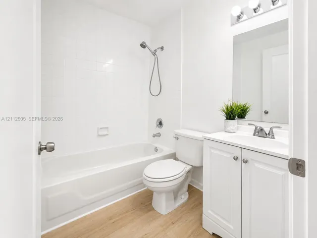 Full bathroom featuring a tub-shower combination with white wall tile, white vanity cabinet with integrated sink, wood-finish flooring, and vanity light fixture