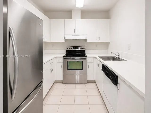 Kitchen featuring white cabinetry, stainless steel appliances, solid surface countertops, a stainless steel sink with a deck-mounted faucet, and ceramic tile flooring
