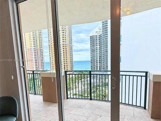 Floor-to-ceiling glass sliding doors opening to a covered terrace featuring natural stone tile flooring and a black metal railing