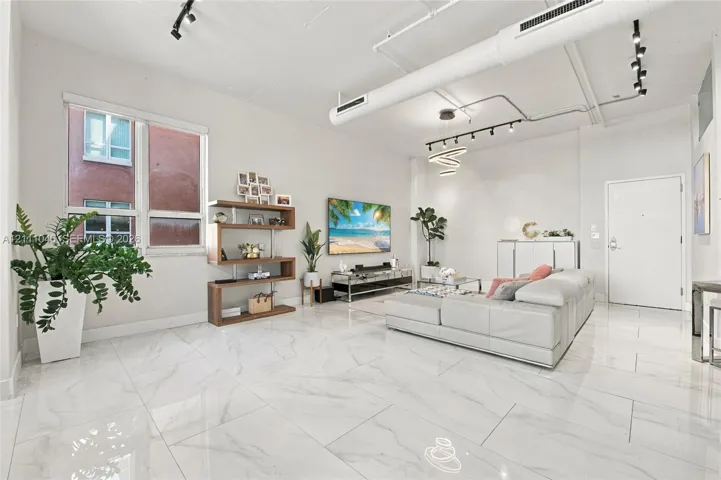 Open-concept living space featuring high ceilings with exposed industrial ductwork, large-format tile flooring, track lighting, and a modern spiral pendant fixture
