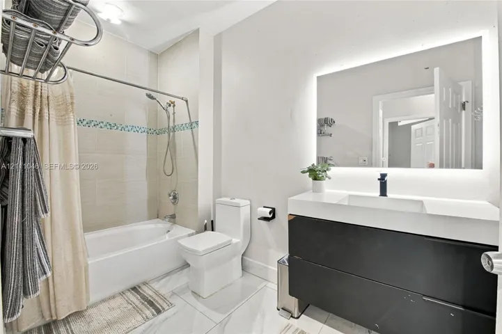 Bathroom featuring a modern floating vanity with a white countertop and dark cabinetry, an integrated LED-backlit vanity mirror, tile flooring, and a bathtub with a showerhead and decorative tile inlay