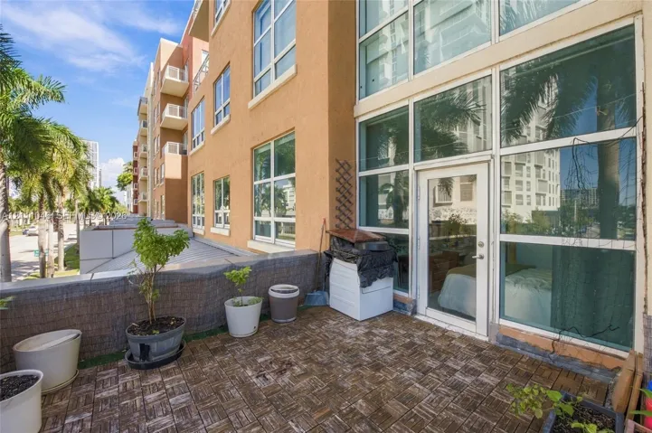 Ground-level terrace with interlocking paver tiles, floor-to-ceiling glass paneling, and a private exterior access door