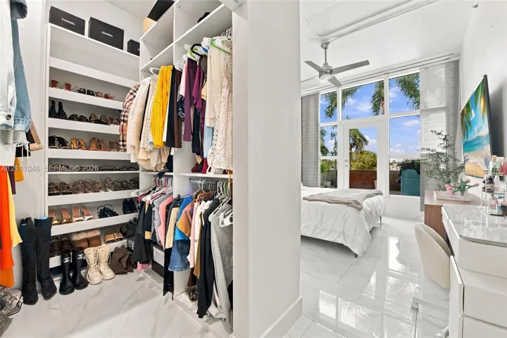 Custom walk-in closet featuring extensive built-in shelving, floor-to-ceiling windows, polished stone-finish flooring, and a sleek ceiling fan