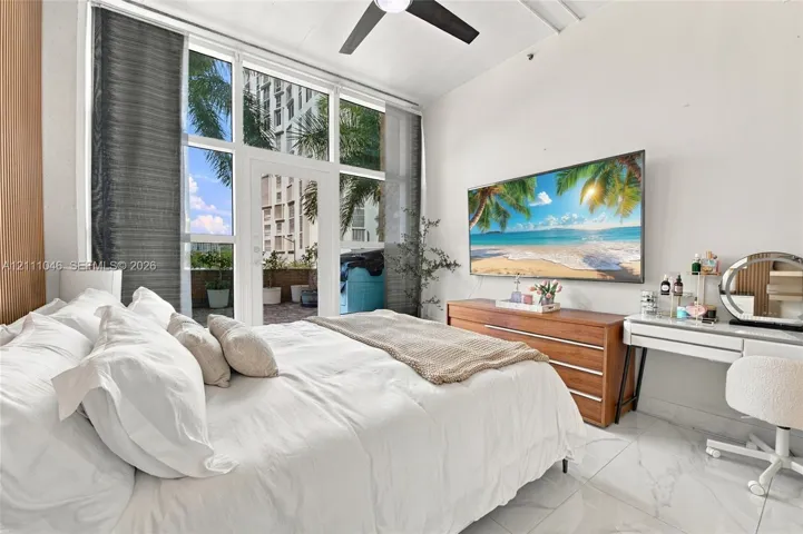 Floor-to-ceiling windows with balcony access, stone-finish tile flooring, and a ceiling-mounted fan