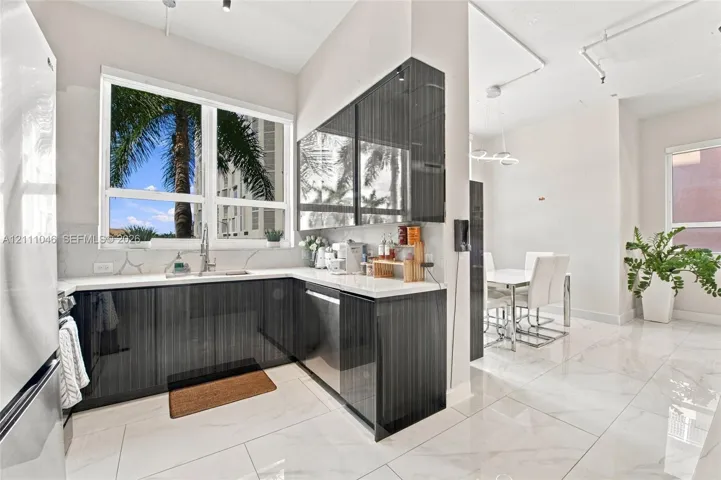 Kitchen featuring high-gloss dark cabinetry, white stone-finish countertops, stainless steel undermount sink, large-format tile flooring, and oversized windows