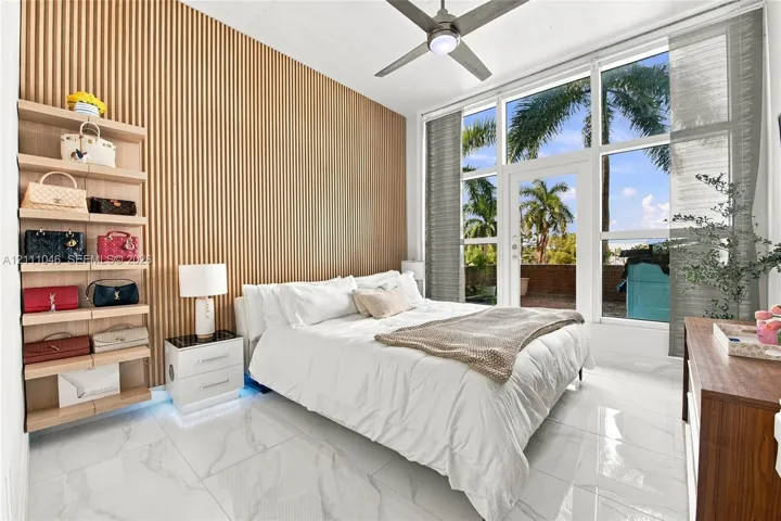 Floor-to-ceiling slatted wood accent wall, expansive wall-to-wall glass windows and door, polished tile flooring, and integrated ceiling fan
