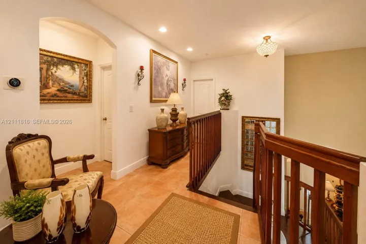 Hallway featuring arched architectural detailing, ceramic tile flooring, a wood-slat banister, and recessed lighting