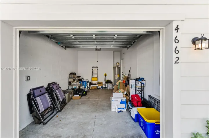 Attached one-car garage featuring a concrete floor, painted masonry walls, an exposed-beam metal overhead door, and a wall-mounted exterior light fixture