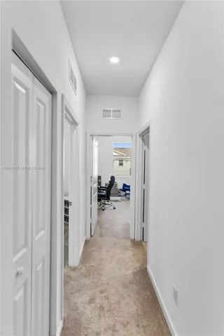Hallway featuring neutral carpeting, recessed ceiling lighting, and multiple interior doorways with white bi-fold closet doors