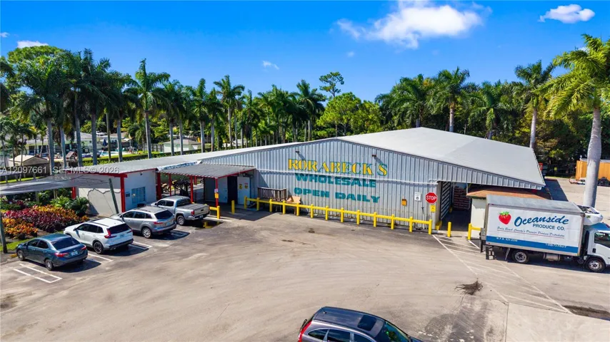 Industrial warehouse facility featuring metal siding, a wide-span gable roof, dedicated paved parking area, and mature perimeter landscaping
