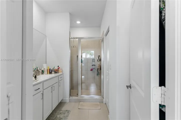 Bathroom featuring a white vanity cabinet with an integrated sink, a large wall-mounted mirror, recessed lighting, and a glass-enclosed shower with tiled interior