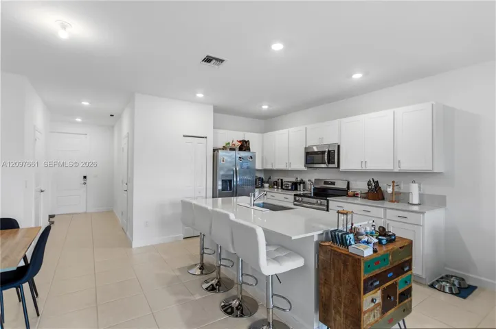 Kitchen featuring white shaker-style cabinetry, a quartz-topped island with seating, stainless steel appliances, and large-format tile flooring