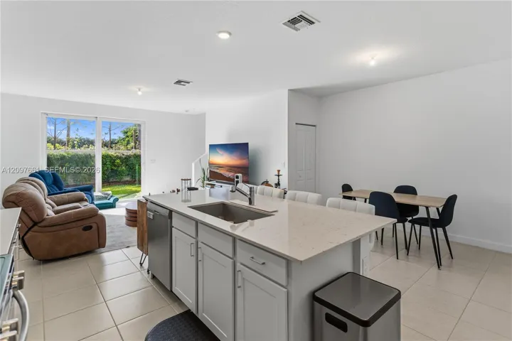 Kitchen island featuring a rectangular undermount sink, stone-composite countertop, and Shaker-style cabinetry, complemented by large-format tile flooring and sliding glass doors