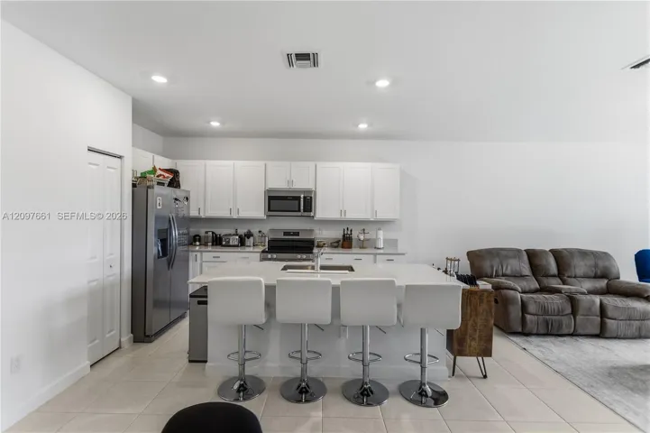 Kitchen featuring white cabinetry, quartz countertops, a central island with an integrated sink, stainless steel appliances, and recessed lighting