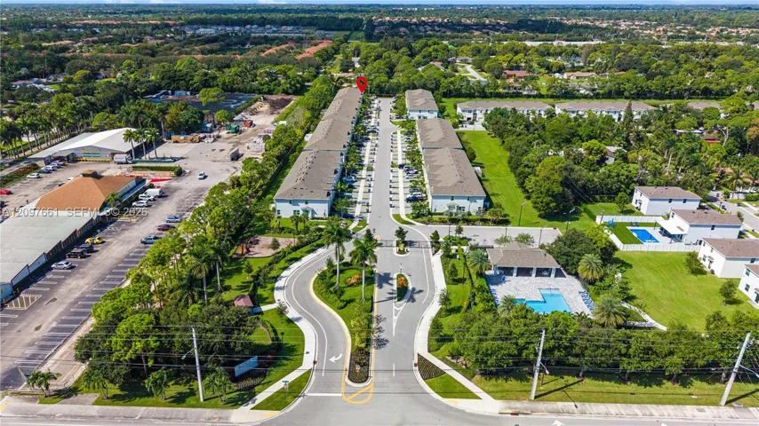 Aerial perspective of the residential complex featuring multi-unit structures with shingled roofing, paved private roadways, landscaped green space, and an outdoor swimming pool