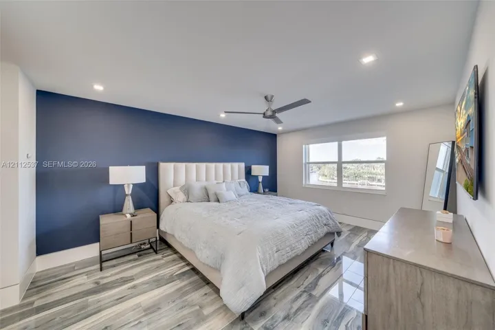 Bedroom featuring a bold navy accent wall, wood-finish tile flooring, recessed ceiling lighting, and a modern brushed-metal ceiling fan