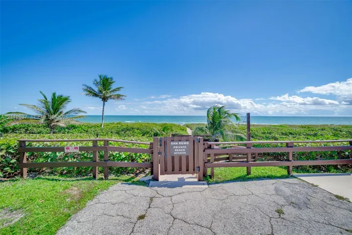 Private beach access featuring a wood-style perimeter fence, secure gate, and tropical landscaping