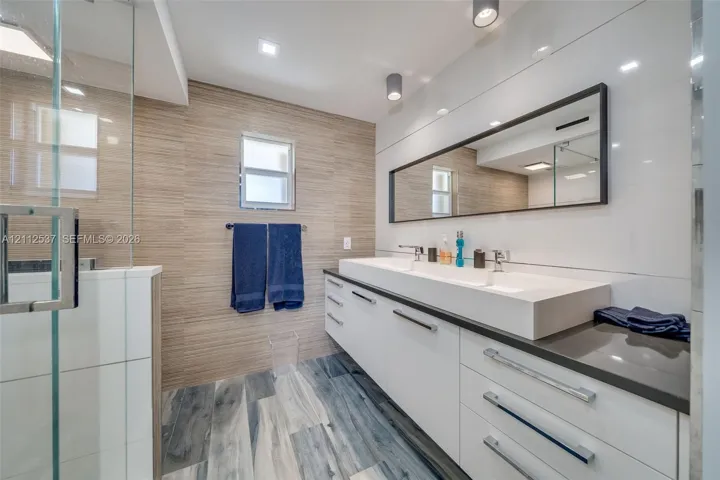 Bathroom featuring a floating double vanity with a rectangular sink, wood-finish flooring, a frameless glass shower enclosure, and full-width wall-mounted mirror