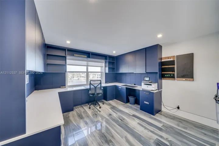 Custom built-in navy cabinetry with integrated shelving, white solid surface countertops, recessed ceiling lighting, and wood-finish flooring