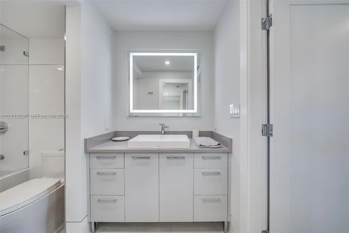 Bathroom vanity featuring flat-panel cabinetry, a rectangular vessel sink, solid-surface countertop, and an integrated LED-backlit mirror