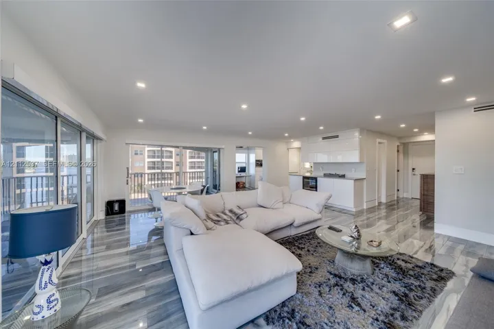 Open-concept living space featuring high-gloss stone flooring, recessed ceiling lighting, sliding glass door access to an exterior balcony, and white cabinetry