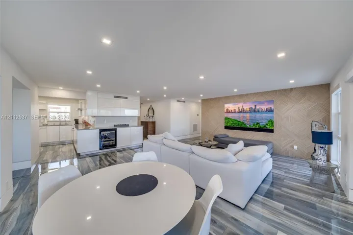 Open-concept space featuring polished stone-finish flooring, recessed lighting, glossy white cabinetry, built-in beverage refrigerator, and a decorative wood-paneled accent wall