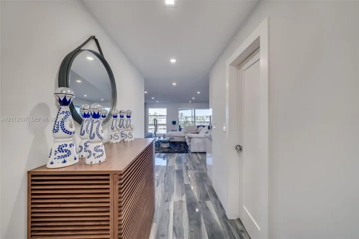Hallway featuring high-gloss, wood-finish flooring, recessed ceiling lighting, and a minimalist door with a polished metallic handle