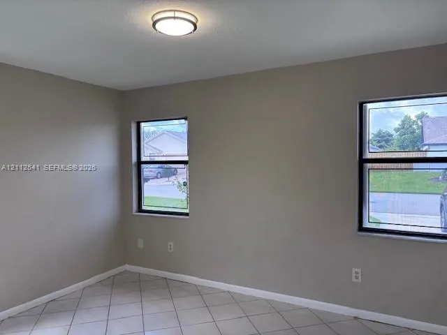 Neutral-toned interior space featuring light-colored tile flooring, flush-mount lighting, and dual windows with black frames