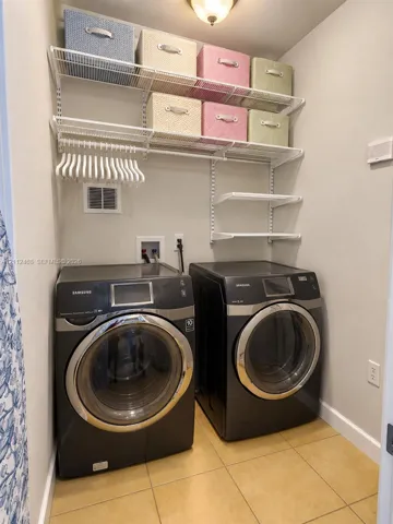 Utility area featuring metal wire shelving, tiled flooring, and dual front-loading appliances