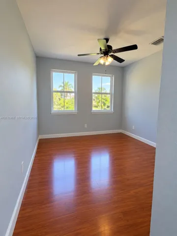Room featuring wood-finish flooring, dual windows with grid detailing, and a multi-light ceiling fan