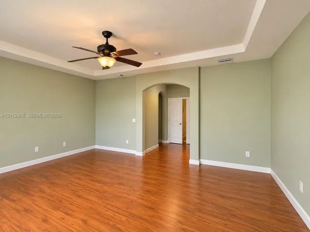 Room featuring wood-finish flooring, a tray ceiling, an arched entryway, and an attached ceiling fan with a light fixture