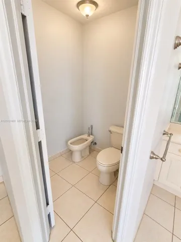 Water closet featuring a two-piece toilet, bidet, neutral tile flooring, and a flush-mount ceiling light fixture
