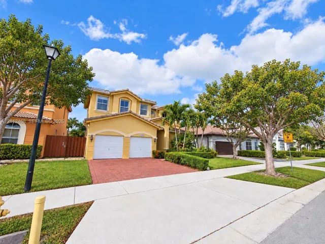 Stucco exterior residence featuring a two-car garage, paver driveway, and tiled roof