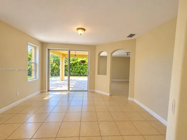 Ceramic tile flooring, arched wall openings, and sliding glass doors opening to a covered patio