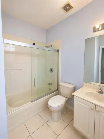 Bathroom featuring a tub-shower combination with glass sliding doors, ceramic tile shower surround, vanity with an integrated sink, and large wall-mounted mirror