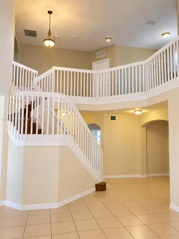 Two-story foyer featuring a vaulted ceiling, prominent staircase with a white balustrade, tile flooring, arched doorways, and a traditional pendant light fixture
